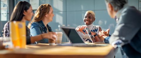 A group of people talking while sitting at a table with laptop devices and coffee cups