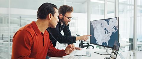 Pair of business colleagues standing in data center reviewing reports on a laptop.