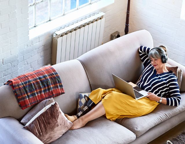 Vista de cima de uma mulher deitada em um sofá olhando para um laptop com fones de ouvido
