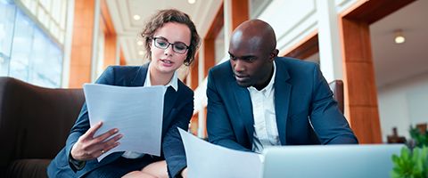 Two colleagues seated at a table in an office looking at documents 