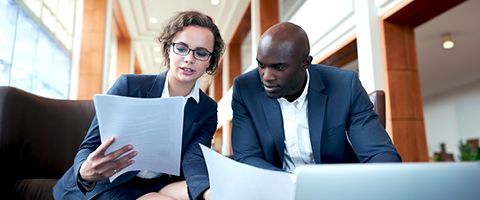 Two colleagues seated at a table in an office looking at documents.