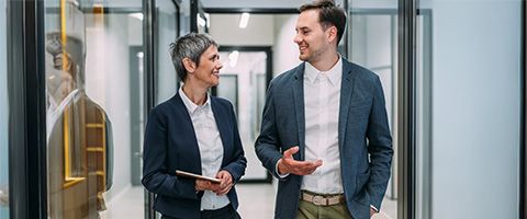 Two coworkers talk and walk with each other through an office setting