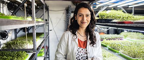 Person smiling and standing in front of shelves of plants.