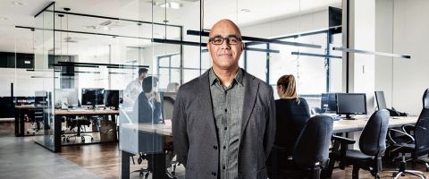 Person in business attire standing in an office setting in front of a conference table.