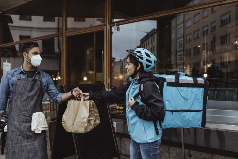 Restaurant worker handing a bag of food to a bicycle delivery person