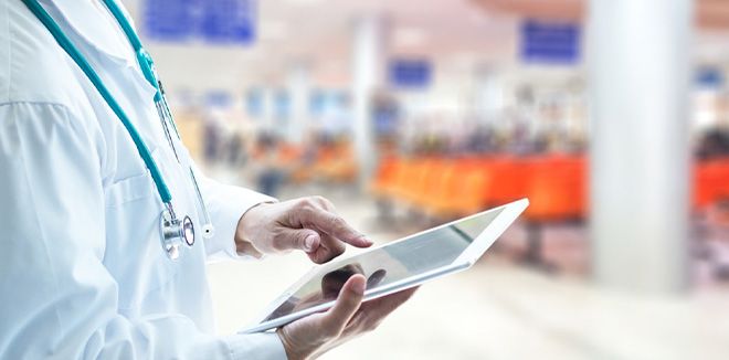 Close up of a doctor's torso in a white coat while working on a tablet device