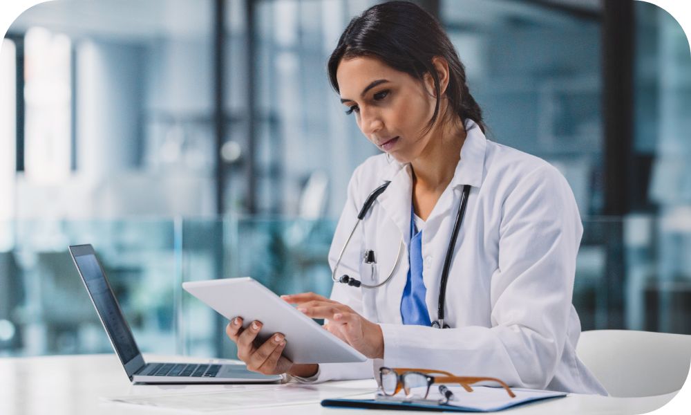 Medical professional working on a smart tablet at a table with a laptop.