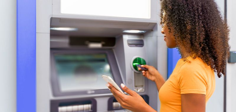 A casual person completes a banking transaction at an ATM machine.