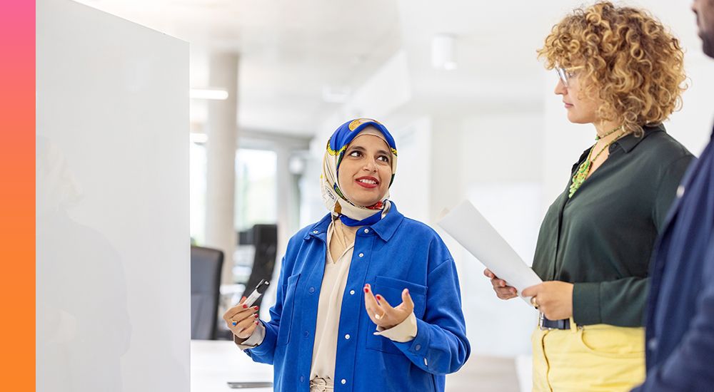 Woman in a head wrap and blue shirt standing and talking to two other people