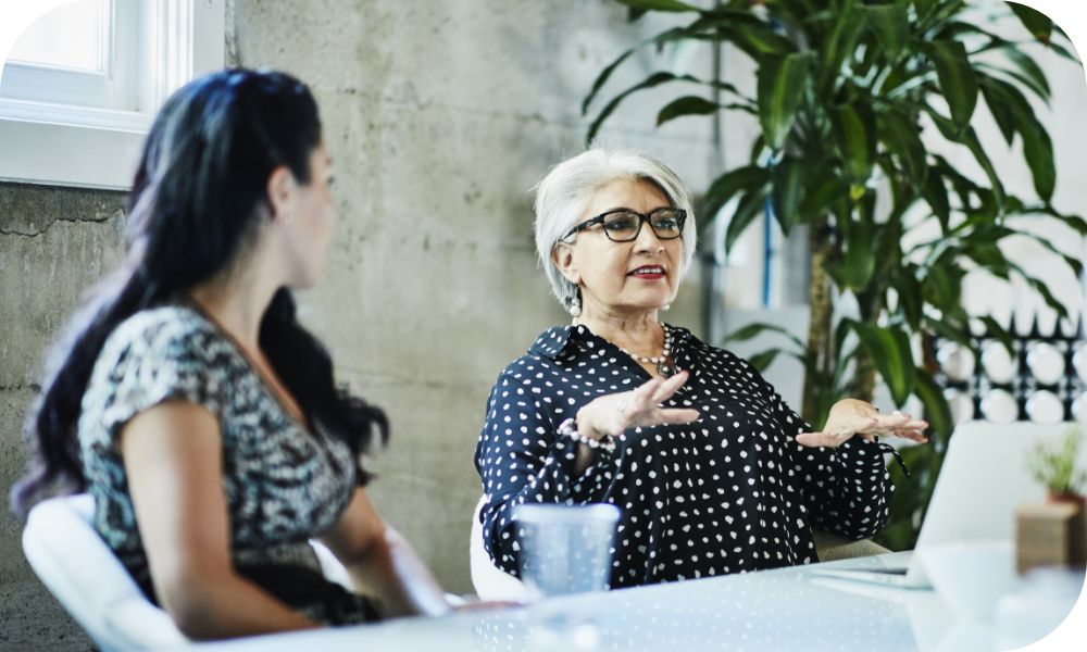 Person talking at a table with two others in an office setting.