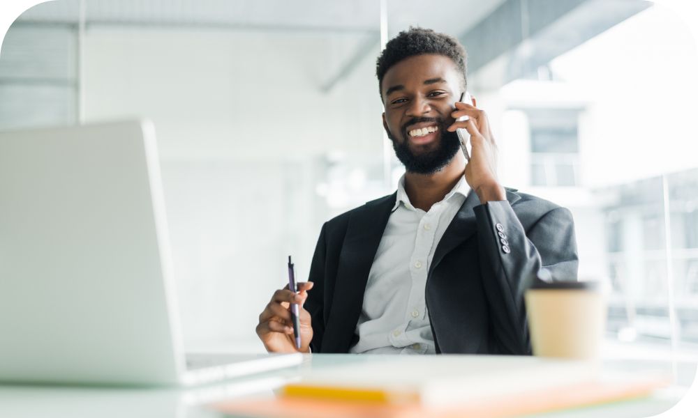 Businessperson talking on cell phone in brightly lit office building with laptop on desk.