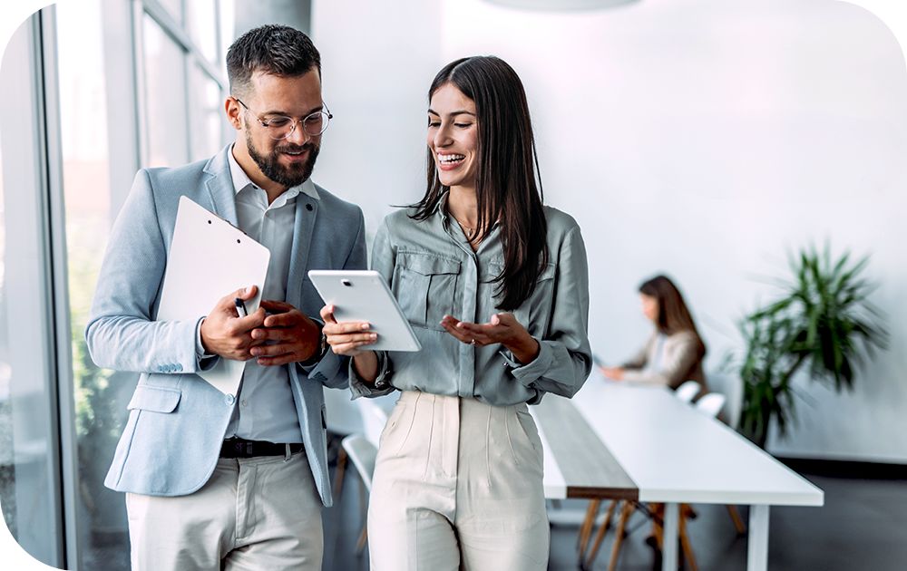 Two businesspeople with computer tables reviewing information as they walk in sunny office setting.