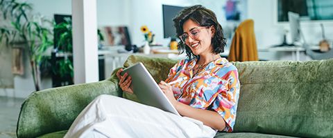 Woman sitting on a green sofa while working on a tablet device in her hands