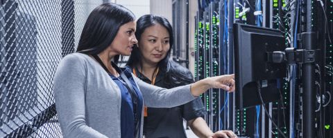 Two people looking and pointing at a monitor mounted on the wall in a data center