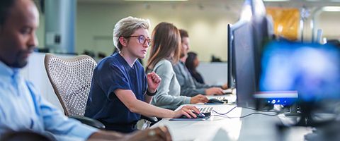 Five people sitting and working at computers in an office.