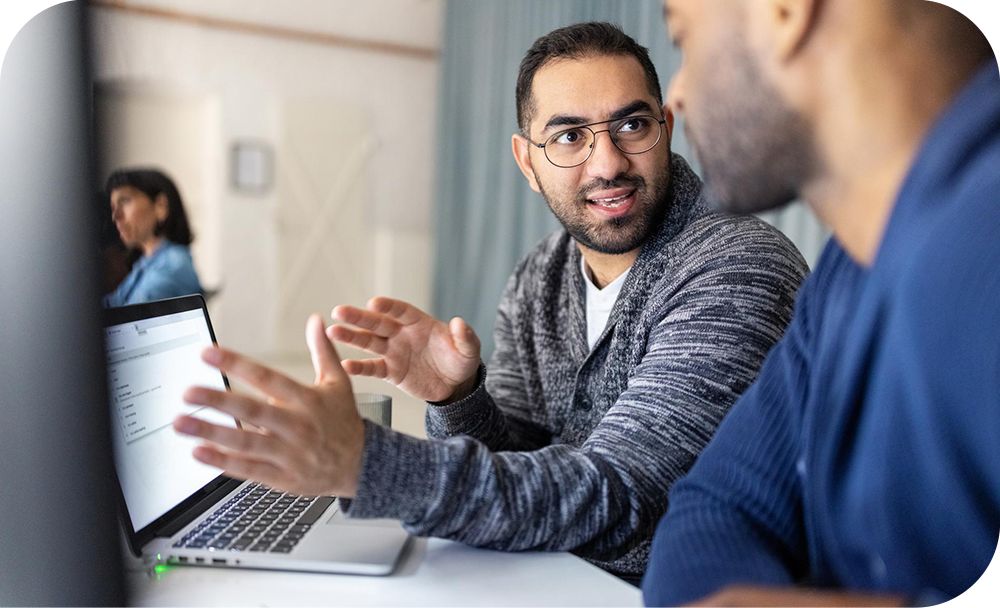 Two people sititng together in front of a laptop having a discussion.