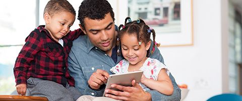 Person sitting with two children looking at a tablet. 