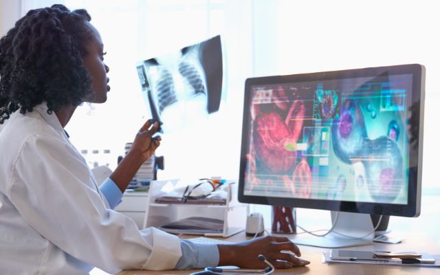 Medical professional holding up an x-ray and looking at additional images on a computer monitor