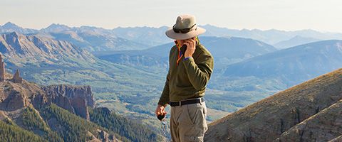 A hiker surrounded by mountains holding a phone connected to the internet