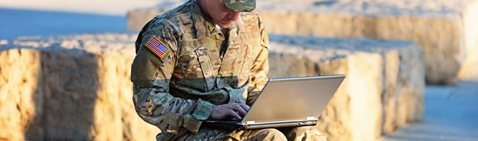 Soldier sitting outside while working on a laptop