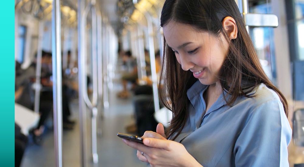 A person uses a smartphone inside a brightly lit subway car with passengers in the background