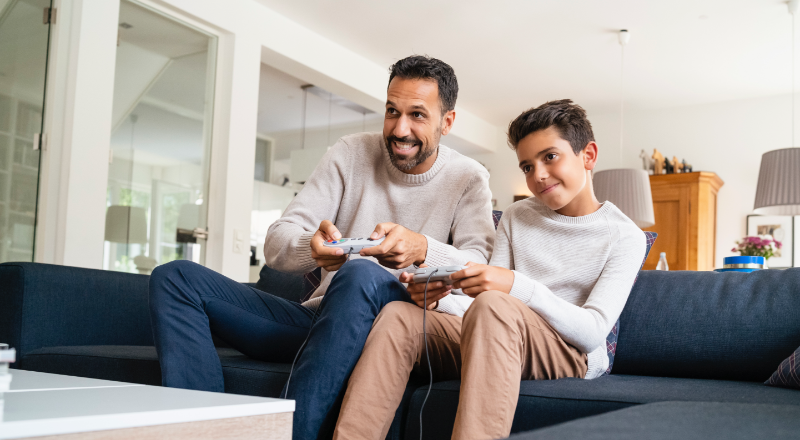 Ein Vater und ein Sohn sitzen auf einer Couch und spielen zusammen Videospiele