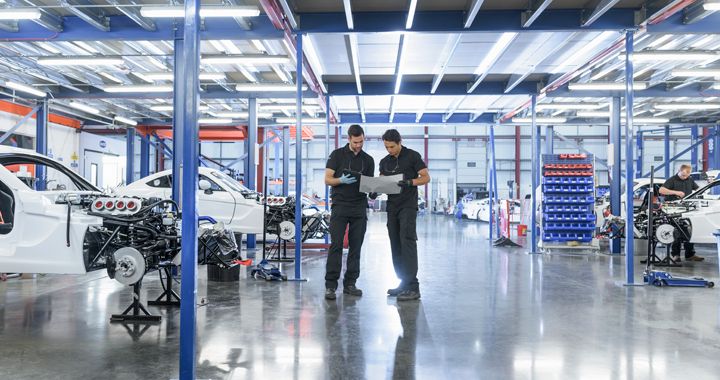 Two mechanics standing in a car manufactoring room looking at designs