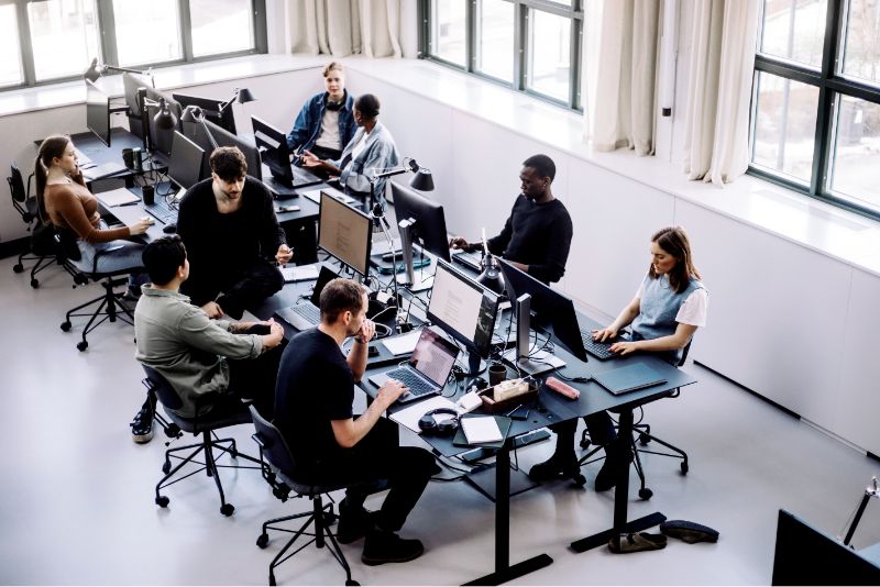 Many people work on computers and collaborate at shared desks.