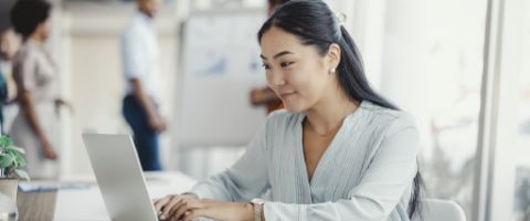 A person in casual business attire works on a laptop in a bright office