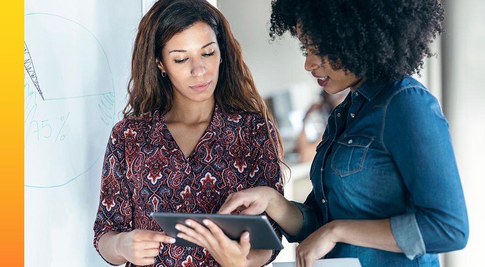 Two women standing while looking at a tablet device in the center of them