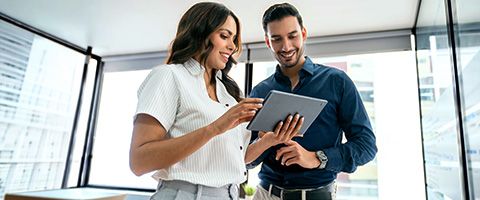 Two people stand next to each other and look at a tablet one is holding.