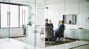 Four business people sitting in a glass conference room