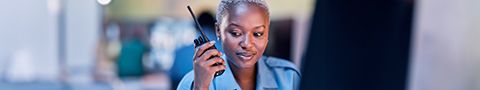 A woman sits in front of a computer while speaking on a walkie-talkie. ______________________________________________