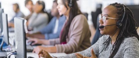 Several people wearing headsets sit in front of desktop computers in a call center 