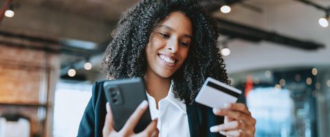 Person in black and white attire smiling and holding a credit card and smartphone. 