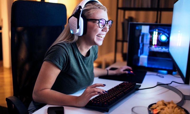 Mujer en casa con auriculares jugando videojuegos con alegría y entusiasmo en un escritorio de computadora.