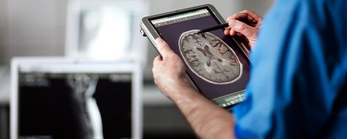 Close up of the back of a someone in blue scrubs looking at an x-ray on a tablet device