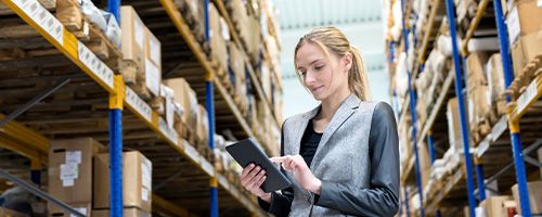 Woman standing in the isle of a warehouse while working on a tablet device