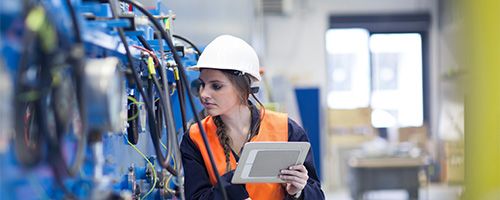 Woman in a hard hat and saftety vest checking equipment with her clipboard