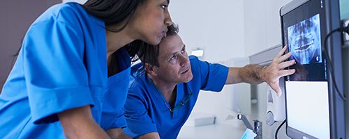 Woman and man in nursing uniforms looking at a screen with an x-ray on it