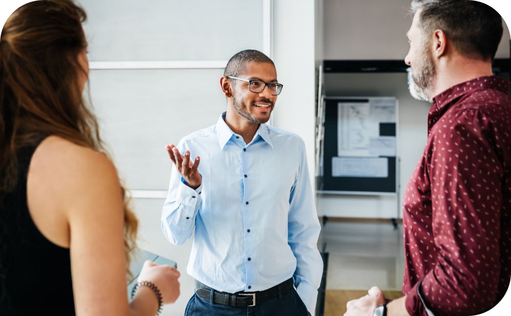 Three coworkers stand facing one another and engaging in a conversation in the workplace