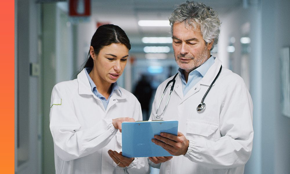 Two doctors standing in a hospital hallway reviewing a patient’s information on a tablet