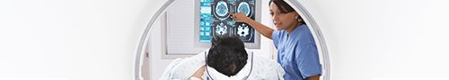 Una médica señala los escáneres del cerebro de un paciente que aparecen en un monitor 