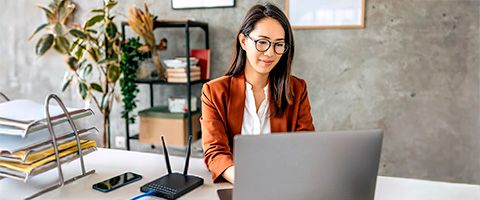 Person in business casual attire sitting at a desk working on a laptop.