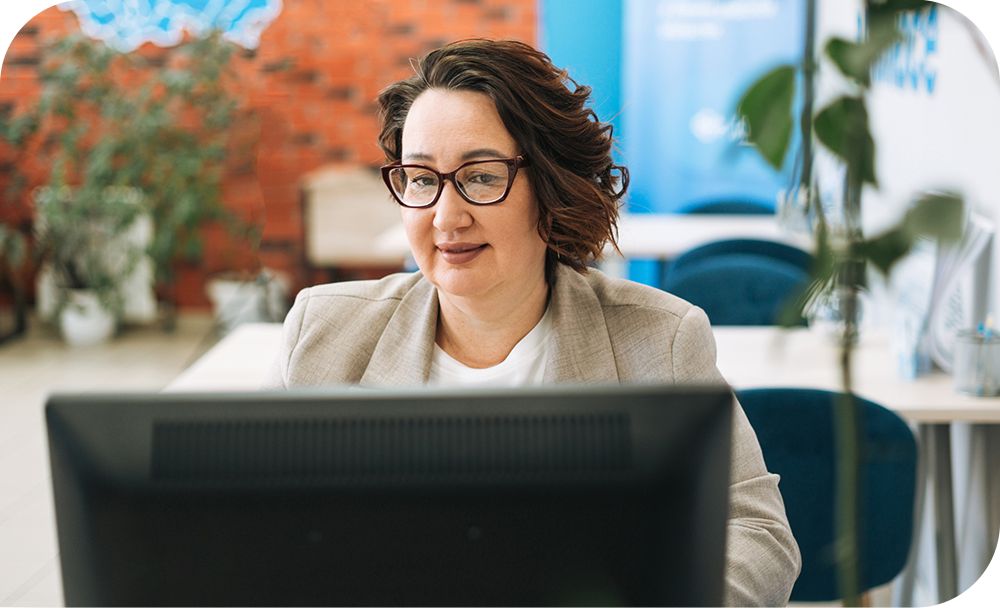 A businessperson wearing a blazer and glasses works on a desktop. 