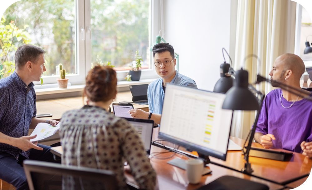 Four businesspeople collaborate at a shared desk.