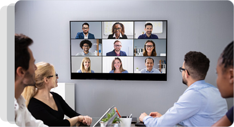 Employees sitting at a table looking at colleagues participating in a video call