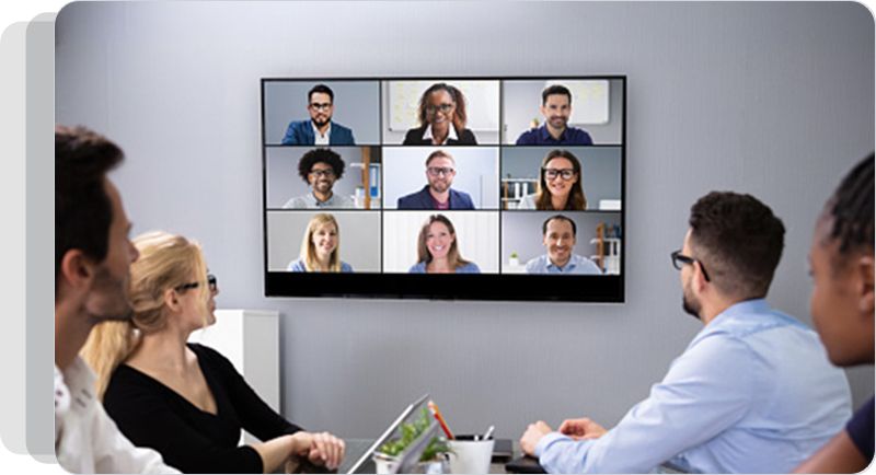 Employees sitting at a table looking at colleagues participating in a video call
