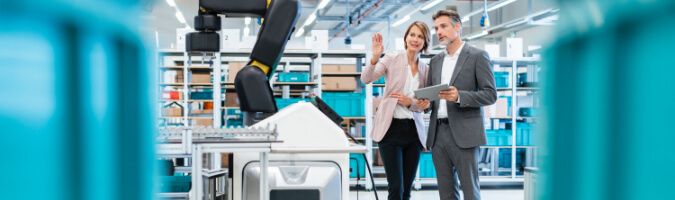 Businesswoman and man holding a tablet control a robotic device in a smart factory