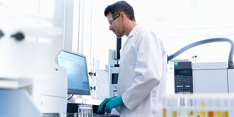 Doctor in laboratory reviewing data on computer monitor analyzing samples from medical vials.